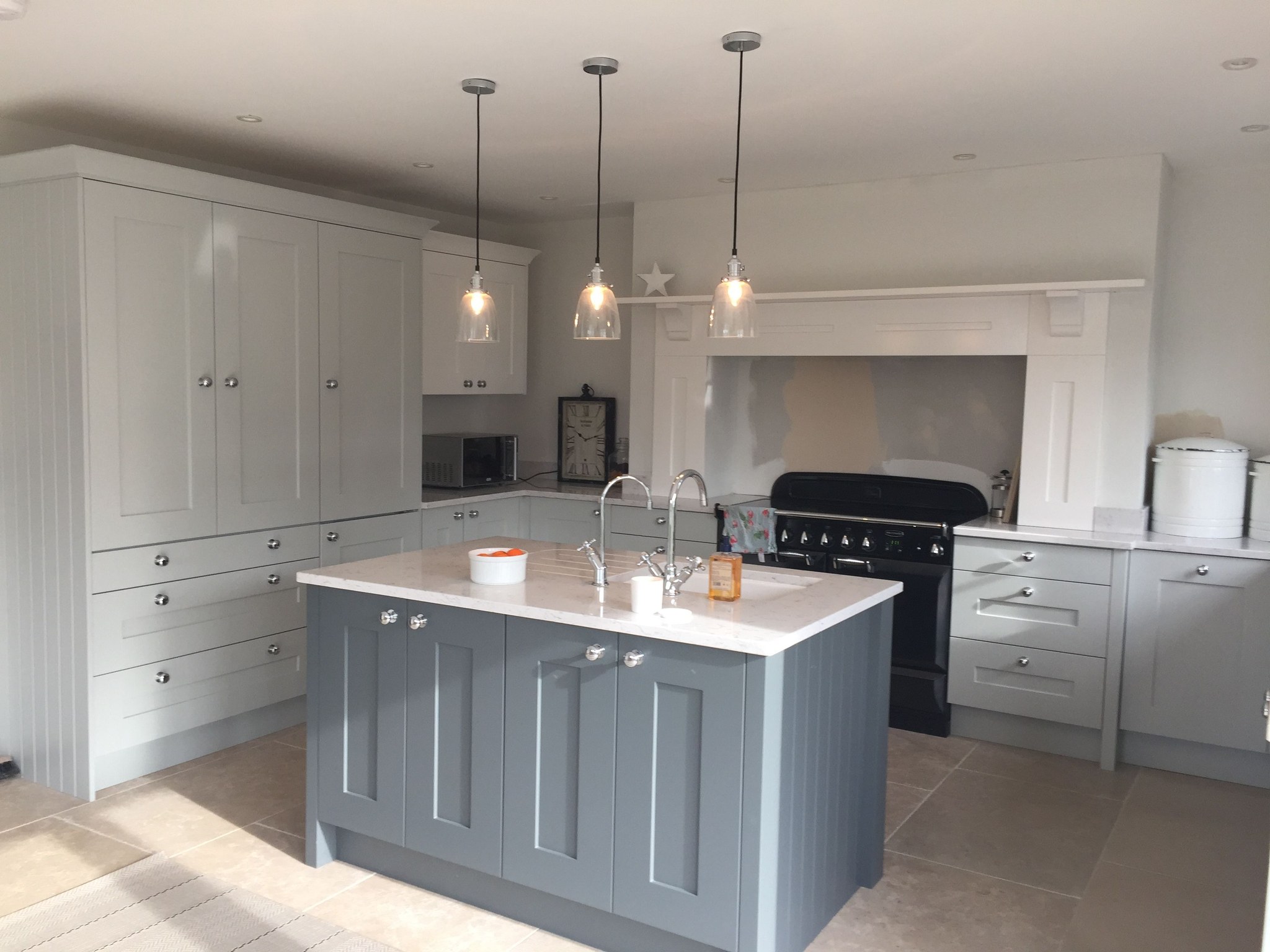 A finished kitchen with a grey painted island, white cabinets and a range cooker