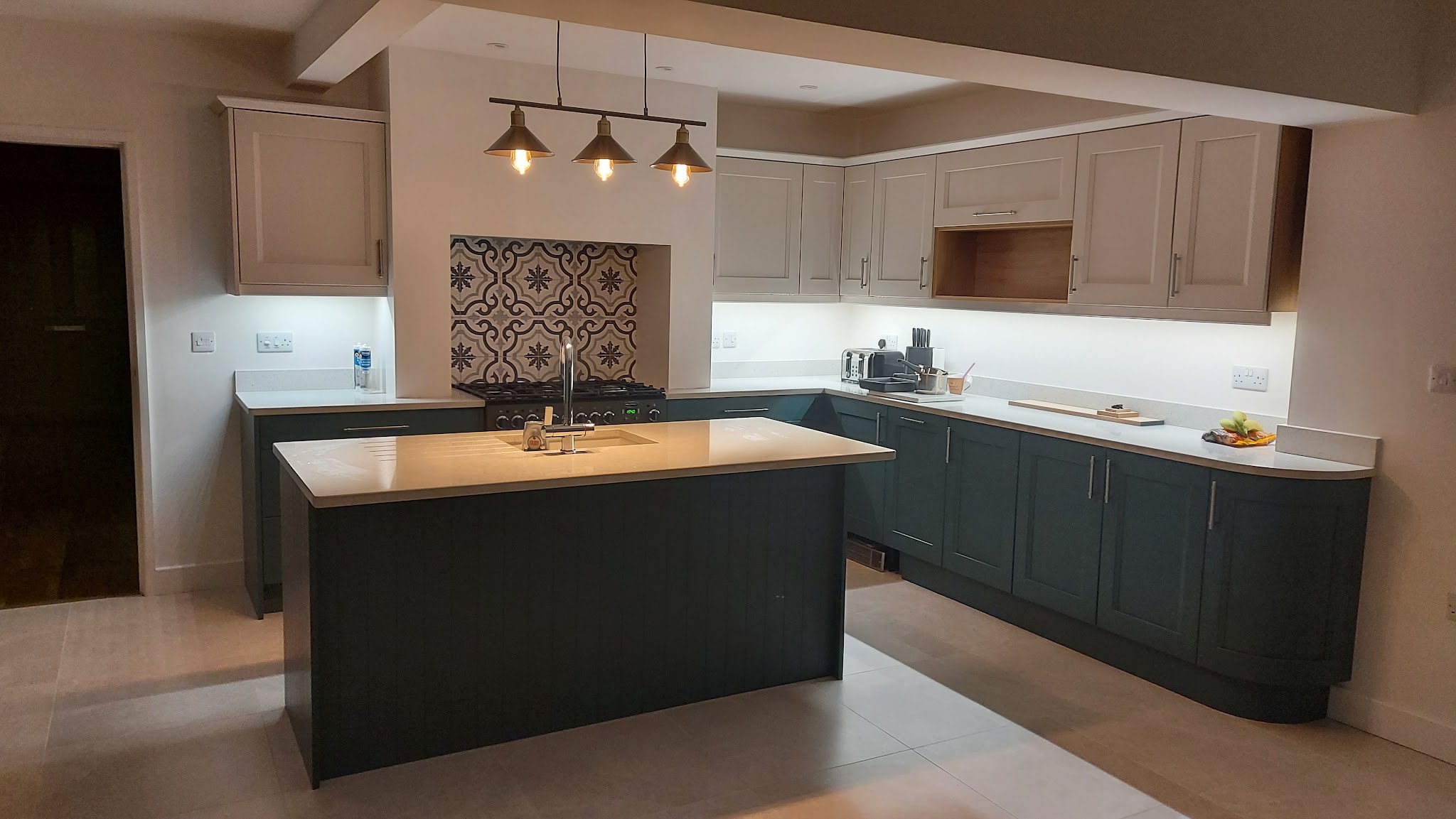 A customer's teal painted island kitchen with a patterned tile splashback and pendant lights